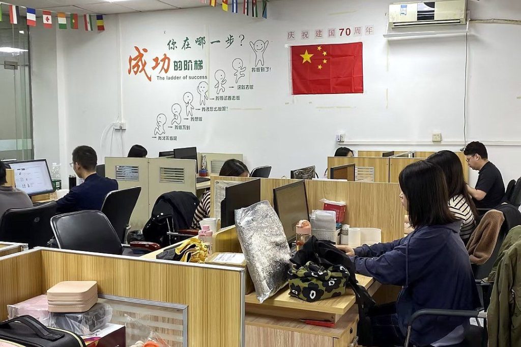 业务办公区,墙上有「成功的阶梯」标语和国旗,工位上放着化妆包等样…