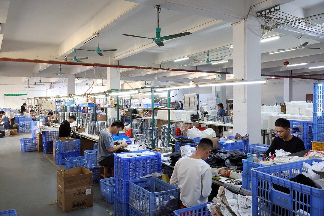 A worker assembling products at an assembly line station, with blue turnover boxes and materials filling the area beside the station