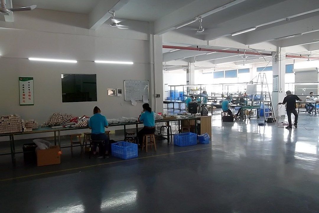 A spacious workshop with multiple rows of workbenches, workers at their stations, and blue turnover boxes beside them