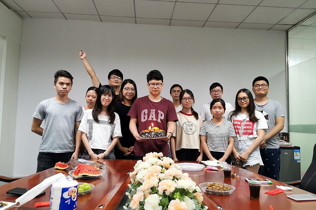 Colleagues gathered around a cake in a meeting room to celebrate a coworker's birthday