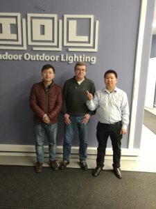 Visiting an overseas customer in front of the IOL (Indoor Outdoor Lighting) company wall.